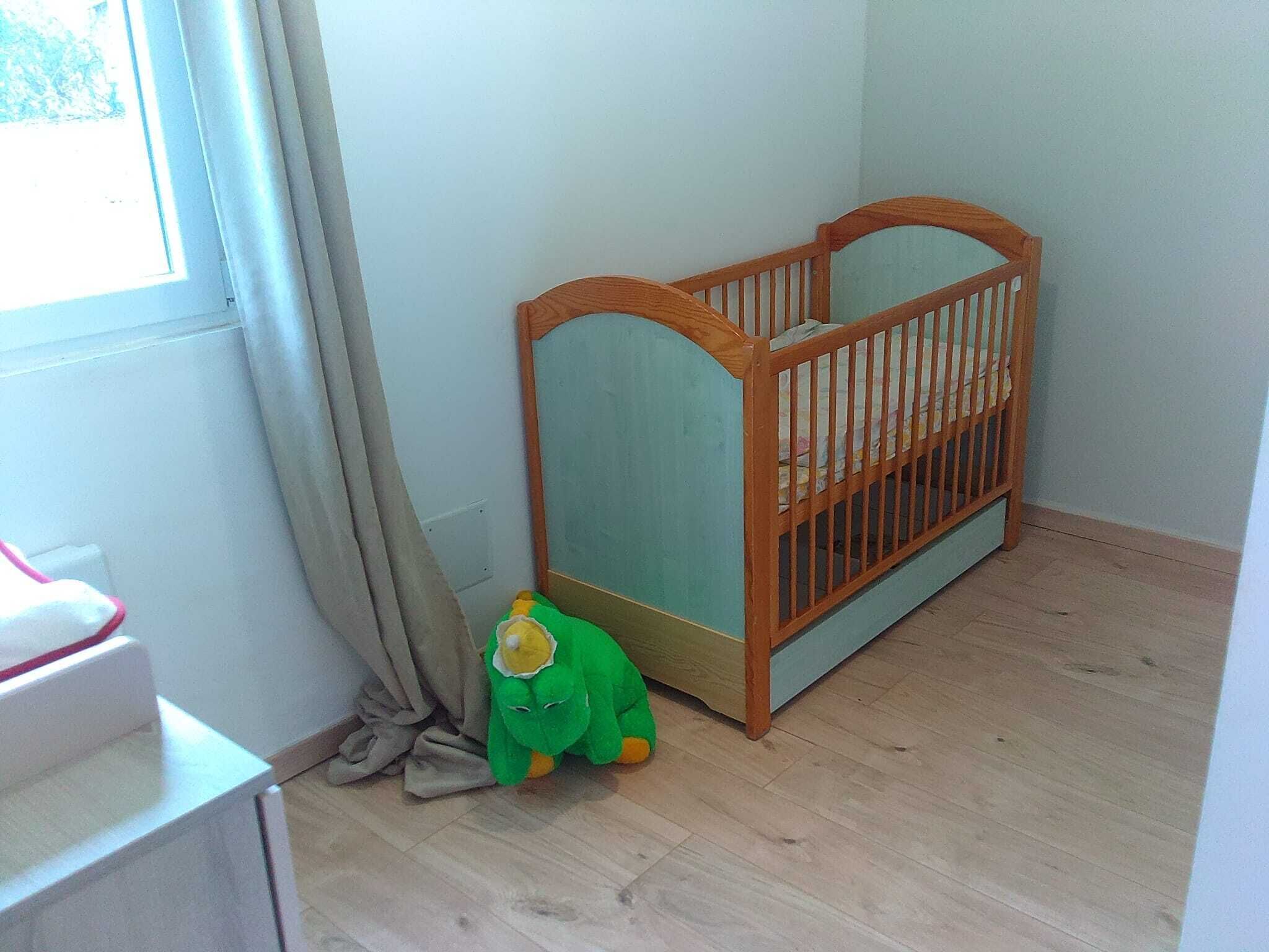 A room with a wooden crib, a small green plush toy, and a window with curtains.
