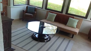 A room with a round glass table, a brown leather sofa with cushions, and a striped rug. - Villa La Ballière: Where memories are written between heaven and earth (Coullons)