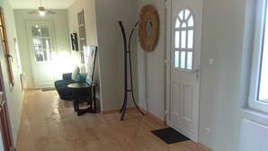 A hallway with a wooden floor, a blue patterned rug, a coat rack, a door with a window, and a dining area with a table and chairs. - Villa La Ballière: Where memories are written between heaven and earth (Coullons)