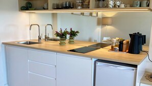 A modern kitchen with a built-in dishwasher, a sink with two faucets, and a countertop with a tablet and a coffee maker. - Suite Milton - Quiet stylish studio in the heart of town, ideal couples getaway. (Milton)