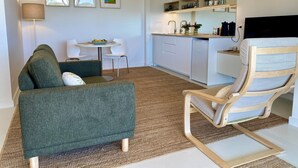 A compact living space with a green sofa, a wooden chair, a small dining table, and a kitchenette area. - Suite Milton - Quiet stylish studio in the heart of town, ideal couples getaway. (Milton)