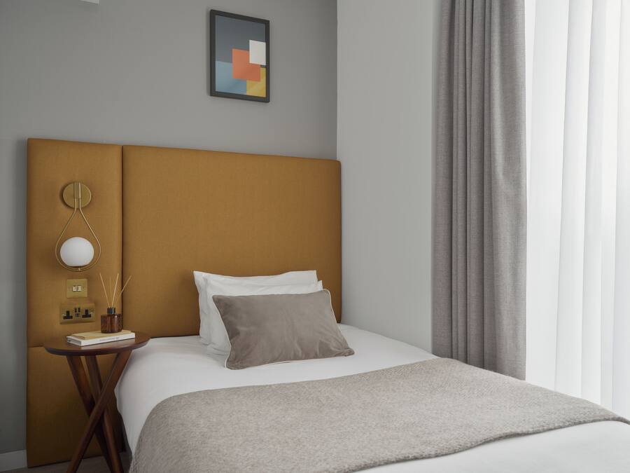A hotel room with a large bed, a bedside table with a lamp, a framed picture on the wall, and a window with curtains.