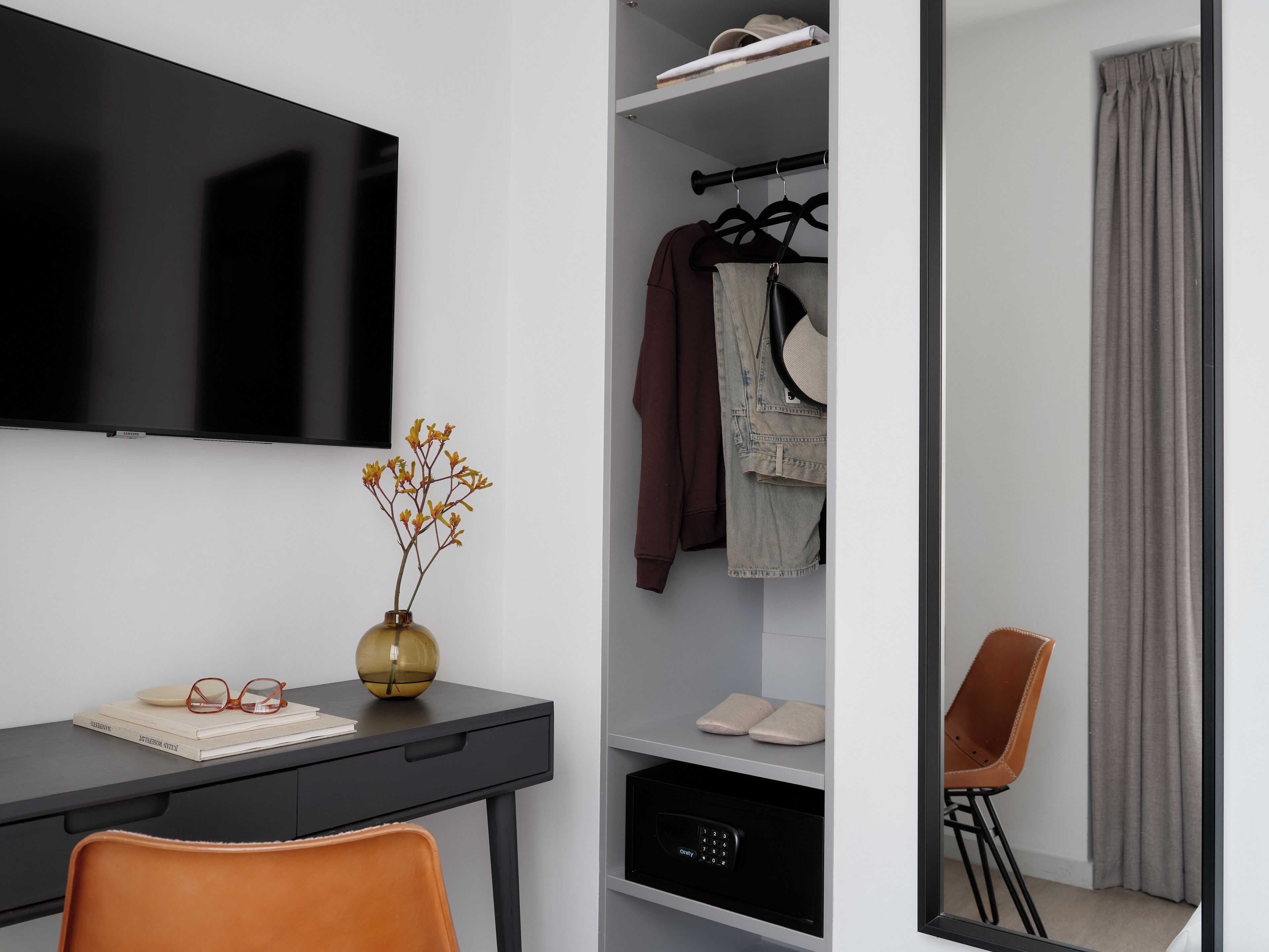 Een moderne kamer met een bureau, een televisie, een kledingkast en een spiegel.