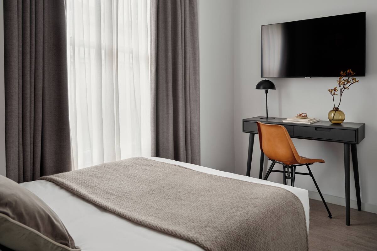 Une chambre d’hôtel moderne équipée d’un lit, d’un bureau avec une chaise, d’une télévision et d’un vase avec des fleurs.