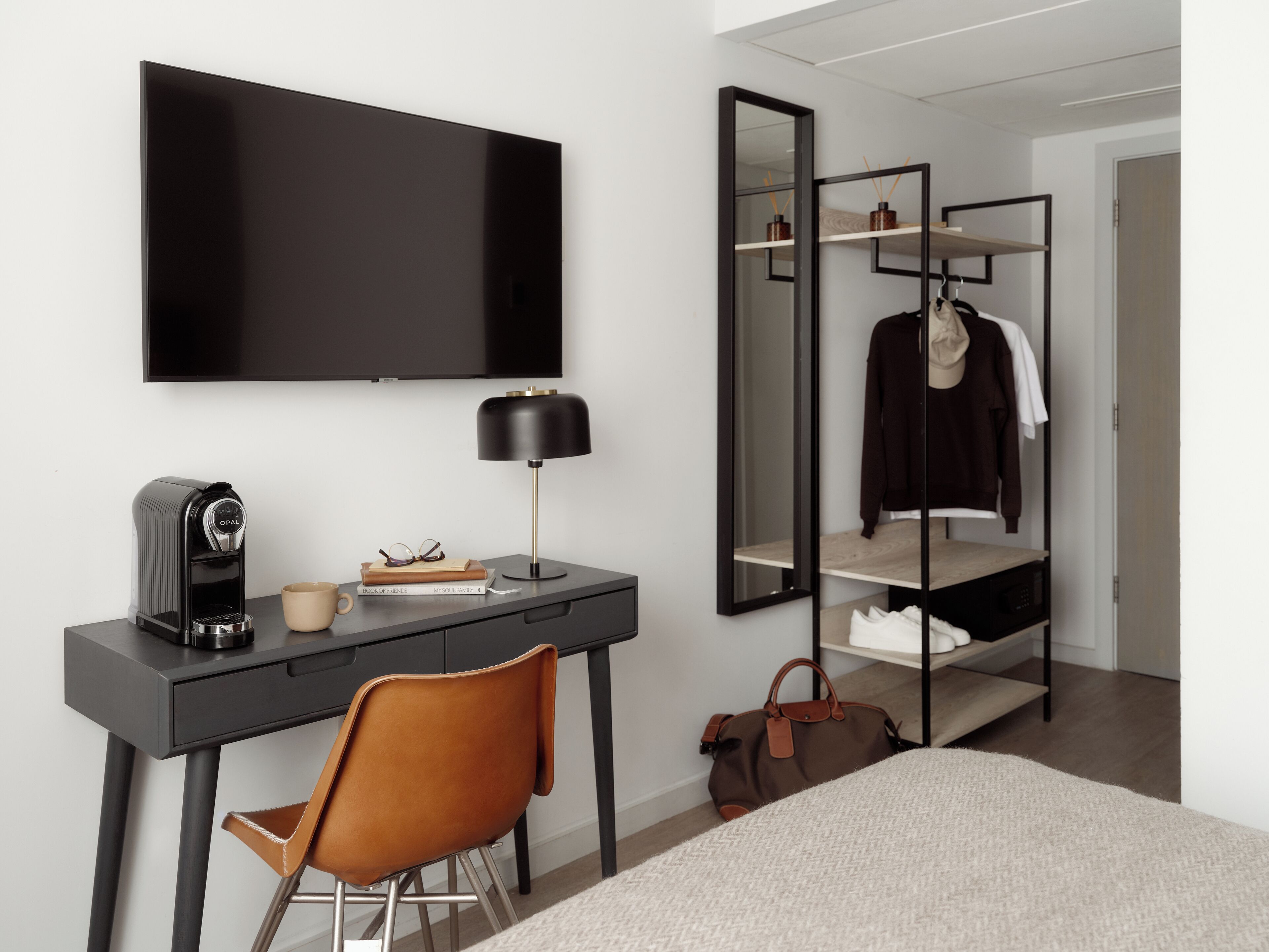 Habitació d'hotel moderna amb televisió de pantalla plana, escriptori amb cafetera, cadira, mirall gran i armari amb prestatges.