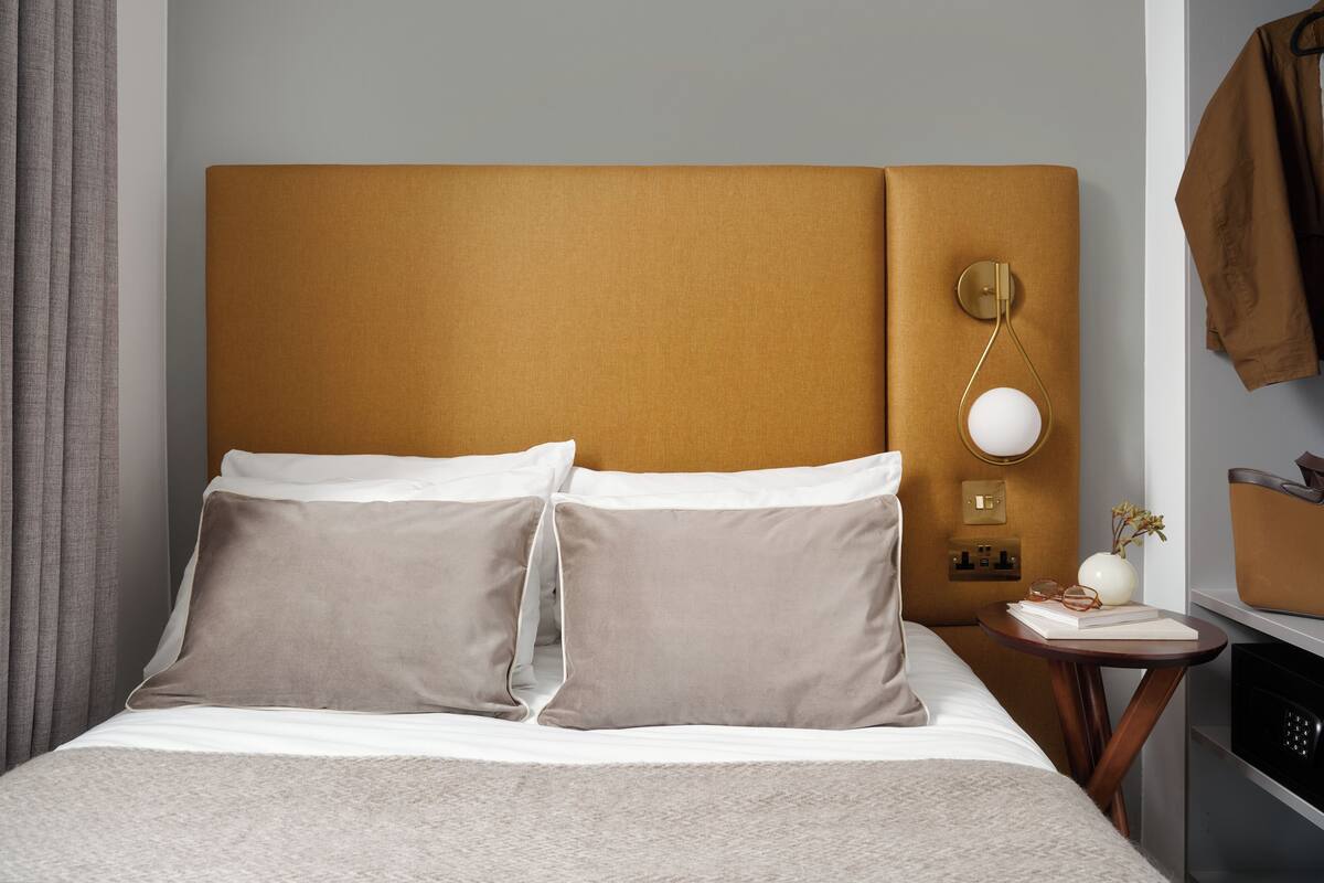 Un lit bien fait avec deux oreillers, une table de chevet avec une lampe et un porte-manteau avec une veste.