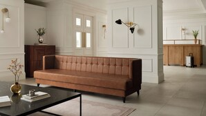 Una sala de estar moderna con un sofá de cuero marrón, una mesa de centro de vidrio y un aparador de madera.