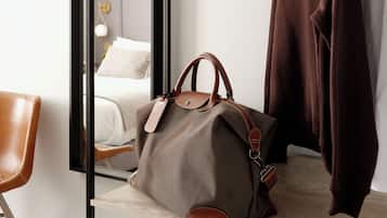 A hotel room with a bed, a wooden shelf, a hanging coat rack, a brown handbag, and a pair of white sneakers.