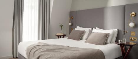 A modern bedroom with a large bed, a bedside table, a nightstand, a wall-mounted light fixture, and a framed artwork.