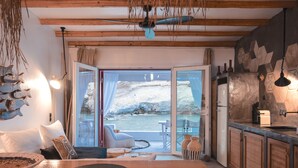 A cozy room with a wooden table, a sofa, and a view of a snowy landscape through a glass door. - Aqua Houses (Milos)