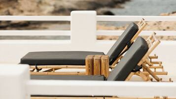 Una silla de playa con cojín negro, estructura de madera y una barandilla blanca al fondo.