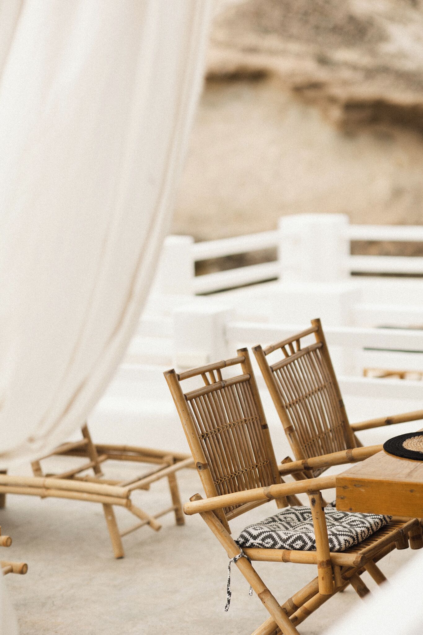 Un entorno de playa con sillas de bambú y una mesa blanca, evocando un espacio al aire libre para comer relajado.