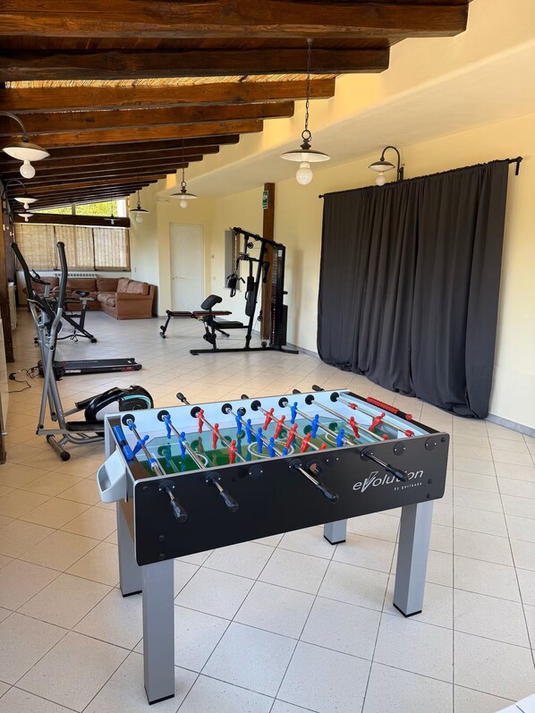 Ein Raum mit einem Fußballtisch, Fitnessgeräten und einer Couch.