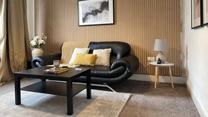 A modern living room with a black leather sofa, a coffee table, and a side table with a lamp. - Stylish Woodhouse Home Near Leeds – Sleeps Ten with Parking Included (Leeds)