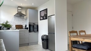 A modern kitchen with a built-in oven, a refrigerator, and a dining area with a wooden table and chairs. - Stylish Woodhouse Home Near Leeds – Sleeps Ten with Parking Included (Leeds)