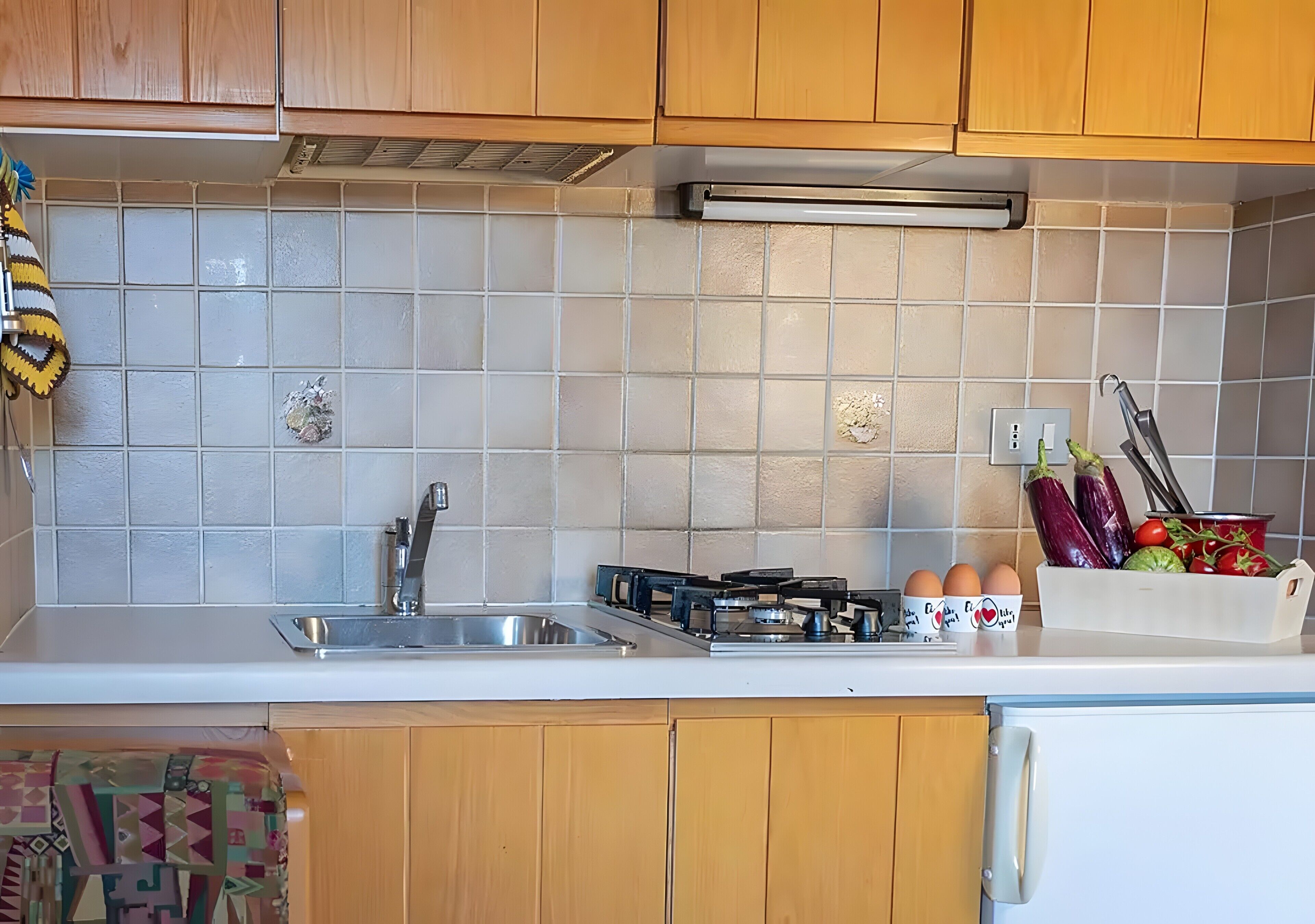 A kitchen with wooden cabinets, a white countertop, a gas stove, a sink, and a fruit basket.