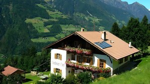 Uma casa de montanha com telhado inclinado, painéis solares e caixas de flores.