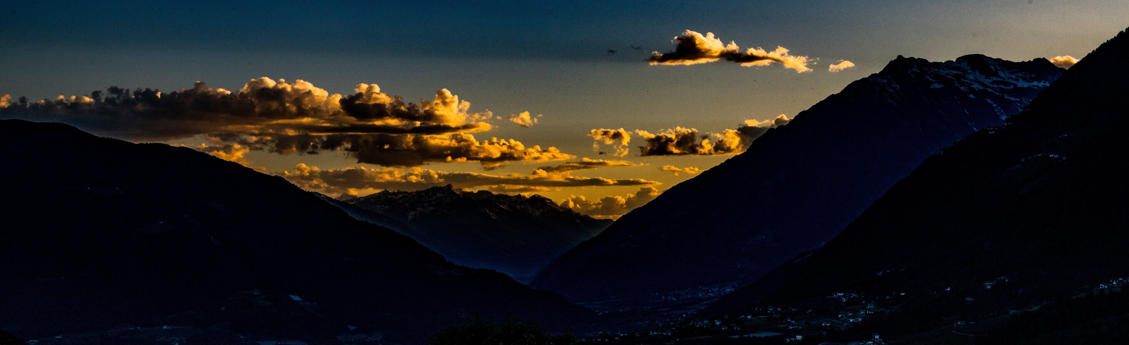 A mountainous landscape with a valley and a body of water reflecting clouds.