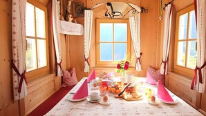 Uma cabana de madeira com uma mesa de jantar posta para o café da manhã, uma cruz e uma janela grande.