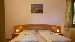 Een tweepersoonsbed met twee nachtkastjes, elk met een lamp, een ingelijste foto aan de muur en een raam met gordijnen.