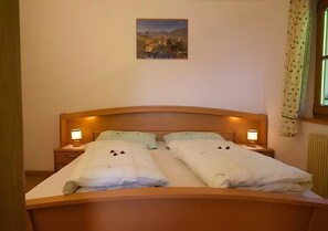 Ein Doppelbett mit zwei Nachttischen, jeweils mit einer Lampe, einem gerahmten Bild an der Wand und einem Fenster mit Vorhängen.