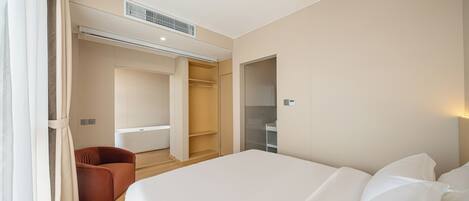 Una habitación de hotel moderna con una cama grande, una zona de estar y un vestidor.