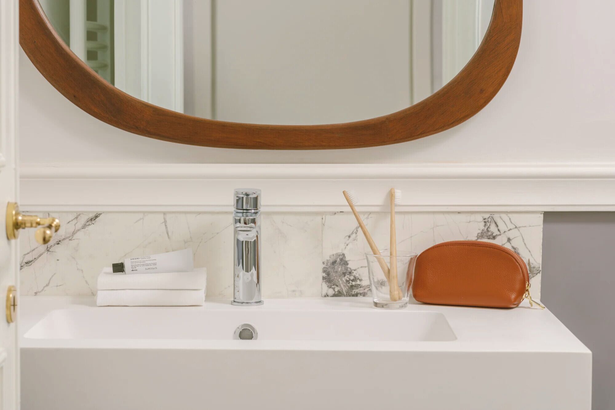 A bathroom sink with a marble backsplash, a round mirror, and toiletries.