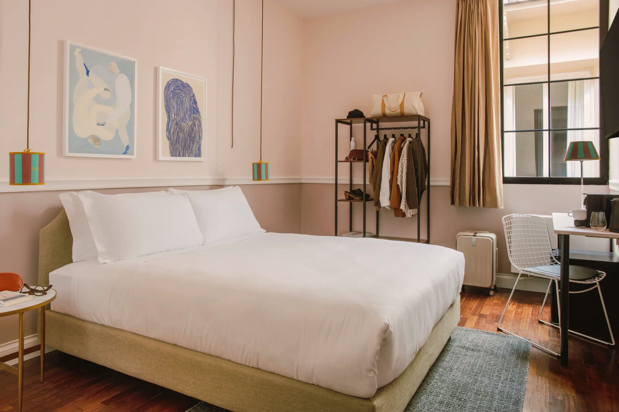 A neatly arranged bedroom with a large bed, a bedside table with a lamp, a chair, and a coat rack with hanging clothes.
