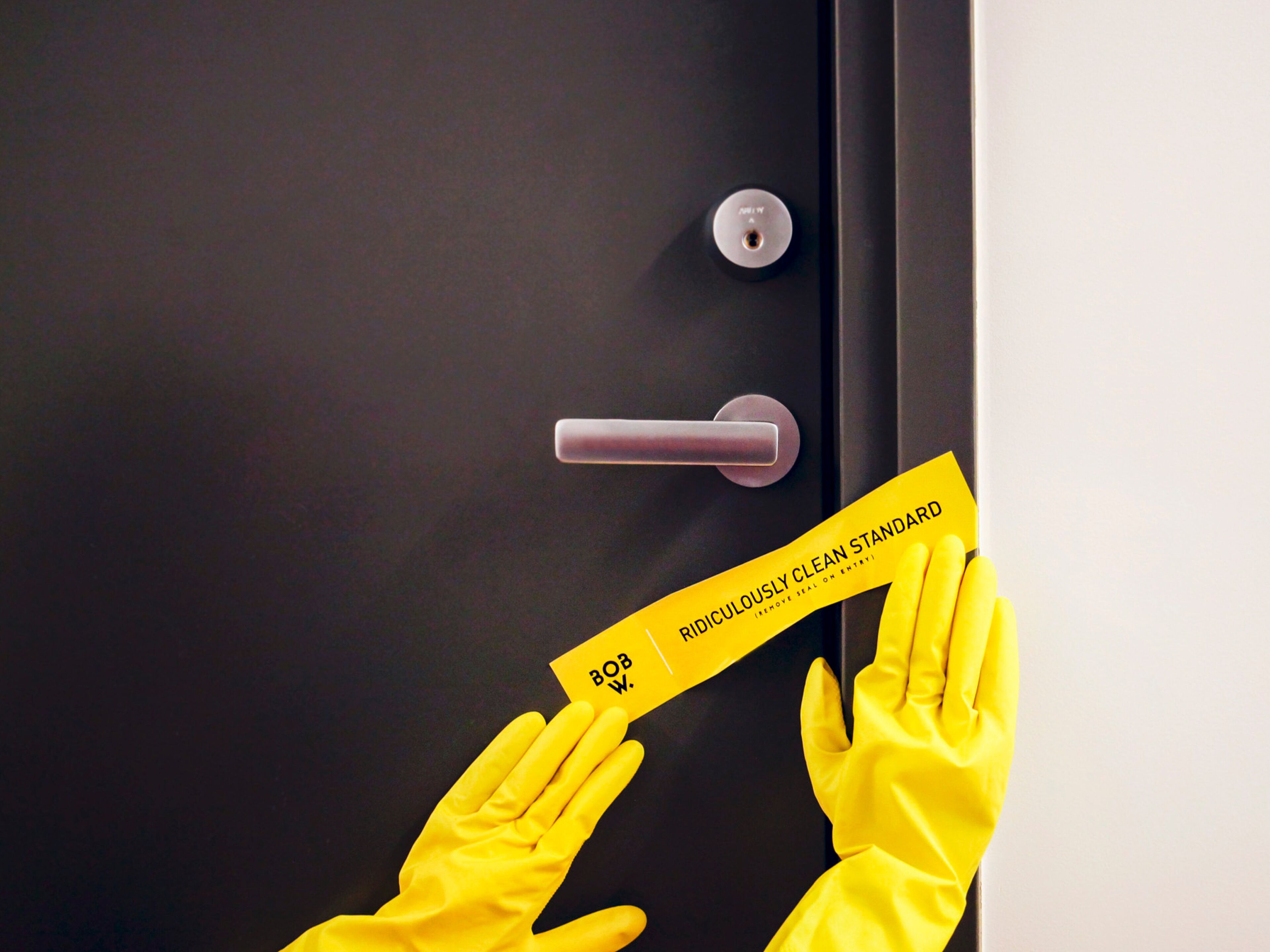 Une personne portant des gants jaunes tient une carte jaune sur laquelle est écrit du texte, et se trouve près d’une porte.