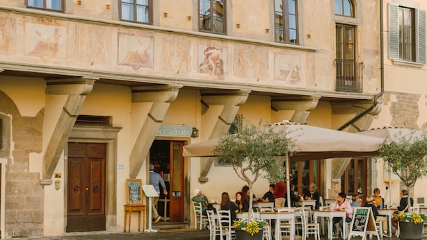 A historic building with arched windows and frescoes, featuring an outdoor café area with tables and chairs. - Bob W Florence Santa Croce (Florence)