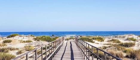 A wooden boardwalk leading to the beach with railings on both sides.