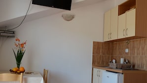 Een compacte keuken met een eethoek, met een aan de muur bevestigde televisie, een kleine koelkast en een betegelde spatwand.