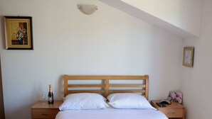 Een slaapkamer met een houten bed, witte kussens en een oranje sprei. Op het nachtkastje staat een fles champagne en een glas. Een ingelijst schilderij hangt aan de muur, en er is een klok zichtbaar.