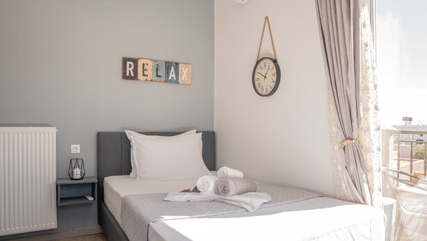 A neatly made bed with rolled towels, a bedside table with a lamp, a wall clock, and a sign that reads "RELAX". - Rodanthi Cretan Villa (Hersonissos)