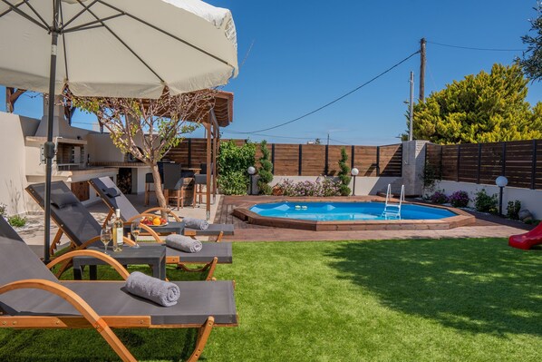 A backyard with a swimming pool, lounge chairs, and a covered seating area. - Rodanthi Cretan Villa (Hersonissos)