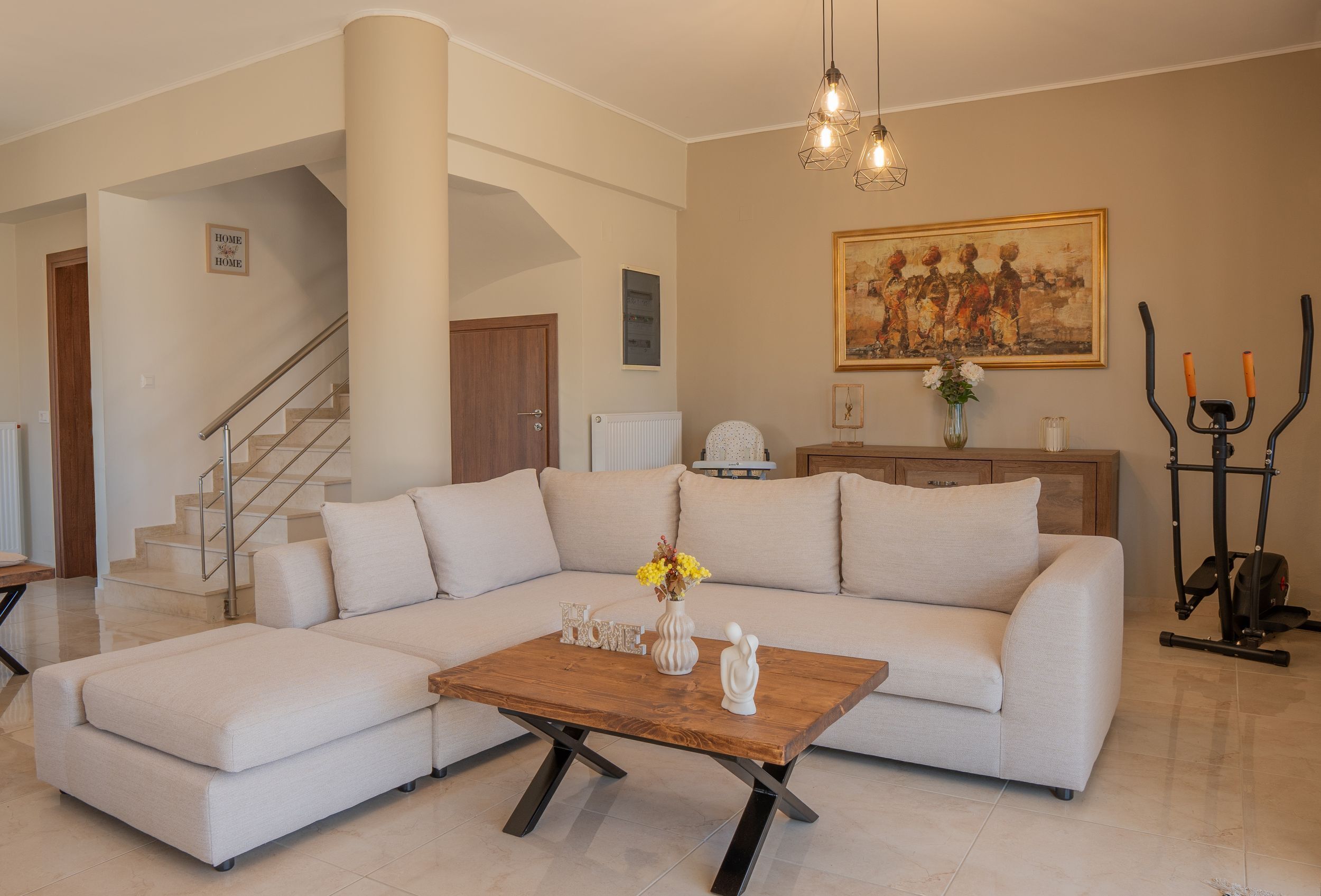 A living room with a sectional sofa, a wooden coffee table, a staircase, and a painting on the wall.