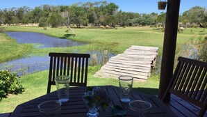 A wooden deck with a table and chairs overlooking a pond and grassy area with trees. - Casa Caracoleni by Interhome (La Paloma)