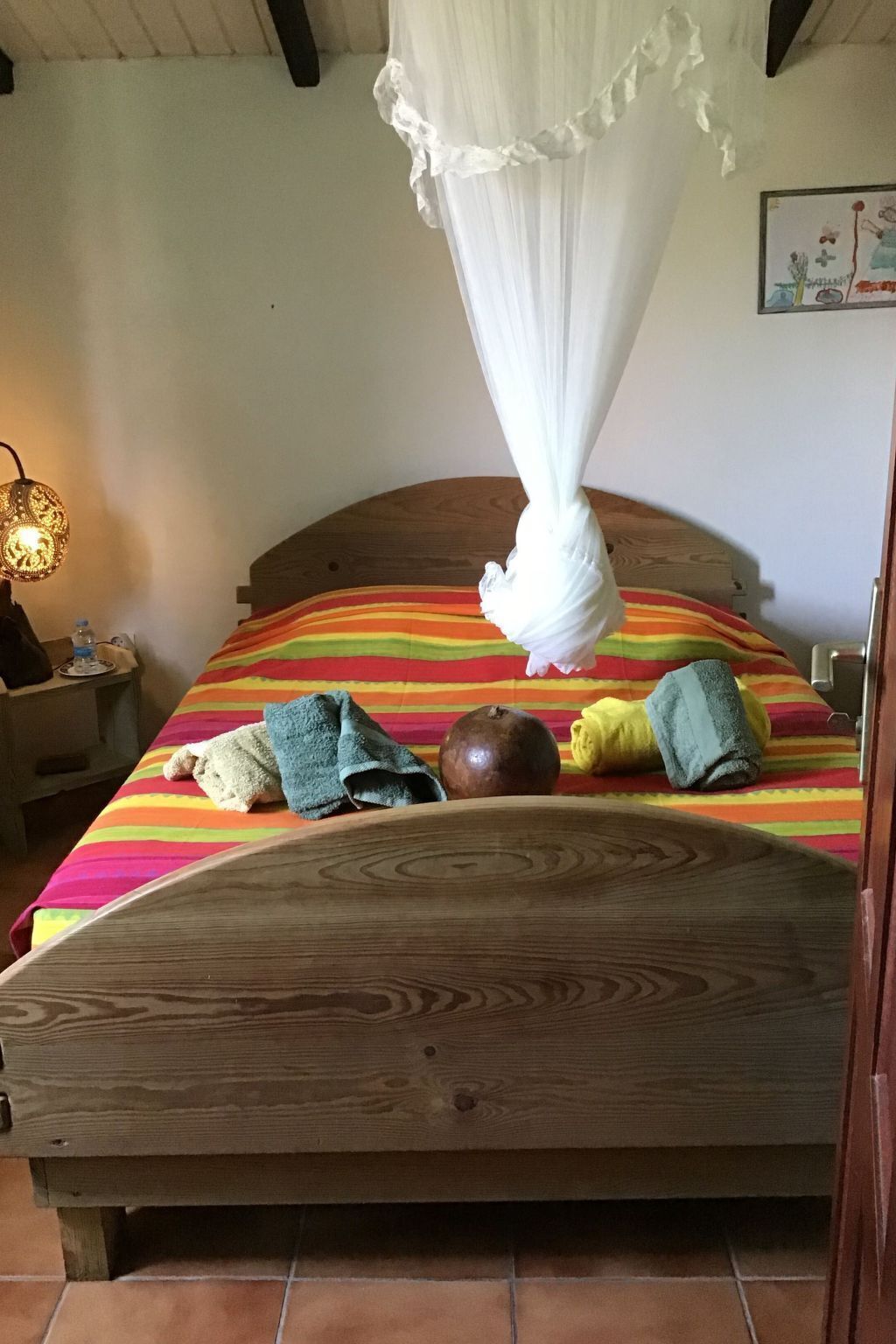 A bed with a striped bedspread, a wooden headboard, and a white canopy. There are towels and a pomegranate on the bed.