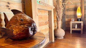 Une sculpture de poisson en bois, posée sur une table dans une cabane aux murs en bois, éclairée par une lampe.