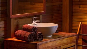 Une salle de bain rustique, avec une cabine en bois, un lavabo blanc, un miroir et un meuble-lavabo en bois.