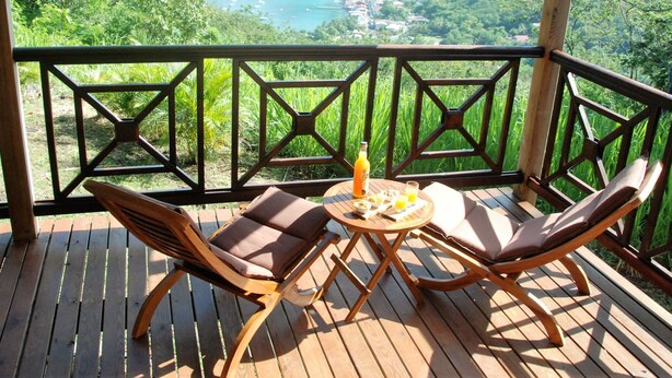 Una terraza de madera con dos sillones de lounge y una mesita, con vistas panorámicas a un lago y montañas.