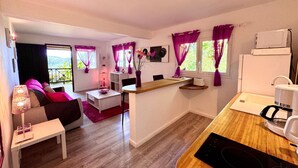 Un espacio habitable compacto con kitchenette, comedor y zona de estar con sofá y una mesa pequeña.