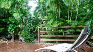 A wooden deck with a lounge chair, surrounded by lush greenery and a wooden fence.