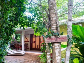 A wooden sign reading "Rouge Coral" in a lush, green outdoor area with a wooden deck and lounge chairs. - Domäne mit Terrasse by Interhome (Deshaies)