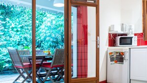 A room with a sliding glass door leading to a patio with a wooden table and chairs, a white refrigerator with magnets, and a microwave on the counter.