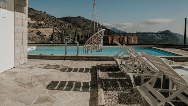 Un espace piscine agrémenté d’un fauteuil suspendu, de chaises longues et offrant une vue sur les montagnes en arrière-plan.