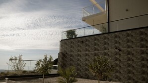 Un bâtiment moderne doté d’une façade en pierre aux lignes géométriques, d’un balcon avec des garde-corps en verre et d’un chemin en gravier agrémenté de petites plantes.