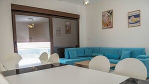A modern room with a dining table, white chairs, a blue sofa, and a large window with blinds.