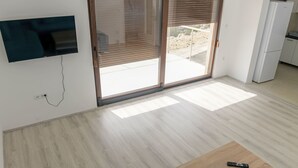 A modern living room with a flat-screen TV, a wooden coffee table, and a sliding glass door leading to a balcony.