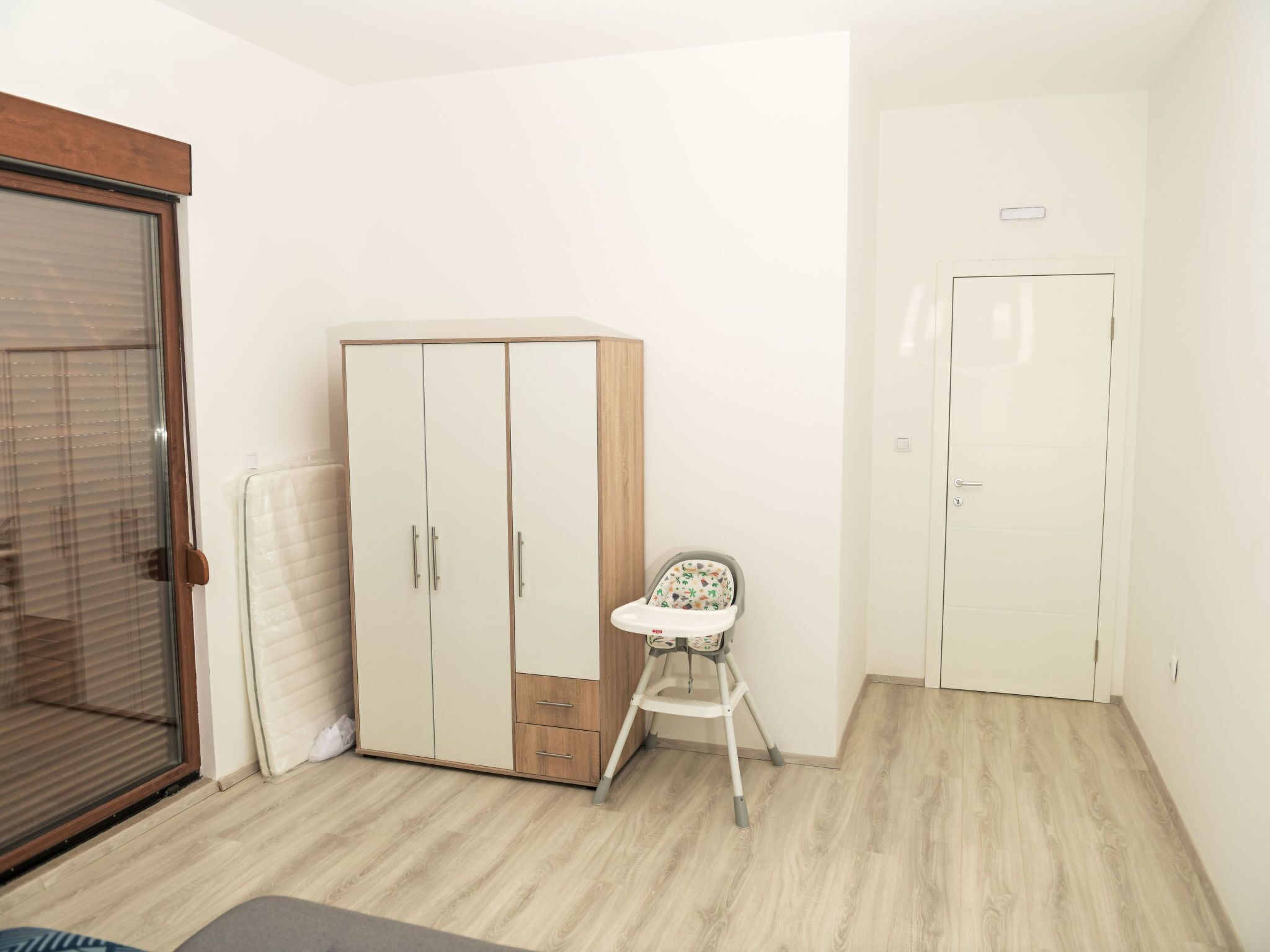 Een kamer met een kast, een kinderstoel en een deur.